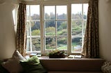 a large window with a desk in front of it. lots of trees and grass and sunshine