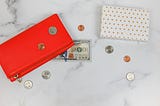 An image of a purse with a few scattered coins and a hundred-dollar bill nearby.