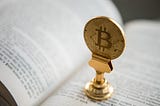 En bitcoin-dekoration som står på sidorna av en öppen bok