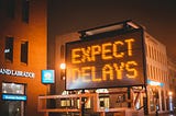 Neon Sign that reads “Expect Delays”