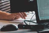 Close up of fingers hvoering over a computer keyboard, with monitors in the foreground