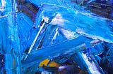 A close up of paint on a canvas with shades of primarily blue, but also white, yellow, and purple. The paint is applied in wide frenzied strokes. The texture of the paint on the canvas is very prominent.