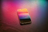This is a photo of an iphone with a colorful screen, sitting on a background that is alsio colorful, mostly reds and pink.