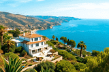 A stunning coastal view in Spain featuring a luxurious villa and sea-view apartment, surrounded by lush greenery under a clear blue sky, highlighting real estate potential.