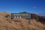 Sign displaying the word “Answers” with a sign telling how many miles to go