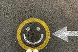 Yellow circle drawn with chalk on black asphalt, with white eyes and smile inside the yellow circle.