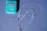 A light blue dental floss container sits next to a strand of dental floss.