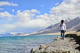 A person in blue jeans and a white sweater stands aloneon a bluff overlooking the ocean