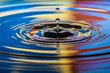A ripple effect created by a stone dropping in water — we see the stone and its colorful ripple effects in water