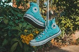 Close up of a pair of light turquoise Converse baseball boots, hanging on a washing line.