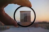 Research section: A magnifying glass held up to show a building as everything on the outside of the glass is blurred out to focus on only the centre of the image where the structure lies.