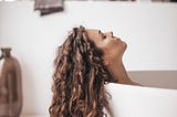 A woman relaxes in a tub with her hair trailing over the edge