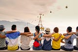 8 children seen from the back, holding themselves by the shoulder to symbolize diversity and friendship, looking at the ocean