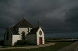 A small, isolated church, against a brooding sky of ominous, dark clouds