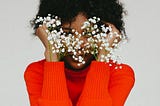 Image of a woman in a bright red top with flowers covering her face.