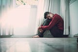 A man sits on the floor, tired, with his eyes closed