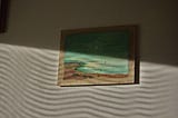 A seaside painting is obscured by wavy shadows on a wall.