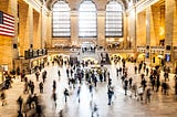 A crowd of people moves through a large, open train station