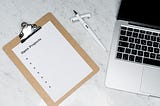 Clipboard with a piece of paper reading ‘open projects’ ready for a list, with a pen and a laptop on a desk