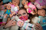 Masked young woman surrounded by baby dolls