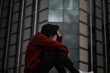 A photograph of a young man sitting alone with his head in his hand. Photo by Cristian Castillo on Unsplash.