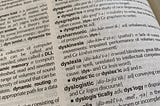 Photograph of a dictionary page from a slanted angle showing the partial definition for dyslexia. The visible part of the definition includes the words: “word blindness” and “unrelated to intellectual competency.”