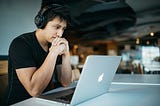 A student at a coffee shop working on a laptop with headphones