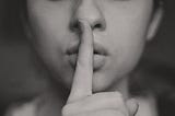 Shh, A face with pointer finger up in front of the mouth, gesturing be quiet, gesturing to be quiet, gesturing to shh.