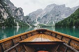 A wooden boat floating in green waters facing a beautiful mountain