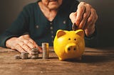 An older person puts coins in a money piggy bank
