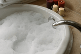 Bathtub filled with bubbles, lit candles and stack of fluffy towels beside tub