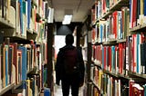 Man walking in a library between bookshelves