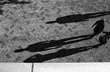 People walking across a sunny square, their shadows stretching before them