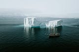 A sailing ship anchored near a massive melting iceberg