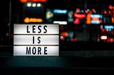 A sign in a window says “Less Is More” against a blurry city backdrop