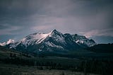 A dramatic mountain landscape featuring snow-capped peaks under a moody sky.