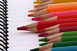 Colored pencils of different sizes on a white notebook.