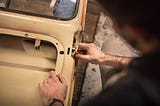 A worker applies what seems to be steel wool to a mechanism on the inner body of a freshly painted automobile.