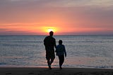 man and girl/young woman walking into a watery sunset with their backs to the camera