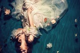 A woman dressed in a white dress floating in the water on her back.