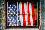 American flag behind a weatherbeaten window frame