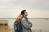 A young couple leaning against each other in front of a beautiful view of a lake.