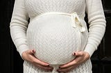 Close-up of pregnant torso in a white sweater holding their baby bump. When a woman is five months pregnant with a baby girl, the cellular beginnings of all of the fetus’s eggs have developed.