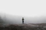 A backpacker stands in front of a forest shrouded in fog