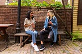 2 females sitting on a bench, with bottles in their hands