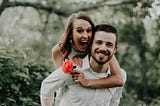 couple in love outdoors, she is holding a flower, both are smiling, image used to illustrate a date night idea for parents