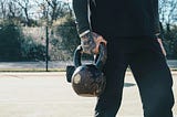 Man holding a kettlebell during an outdoor workout for strength training and fat loss.