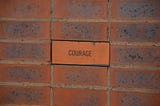 A picture of an orange-brown brick wall, with the center brick written ‘COURAGE’