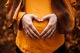 A woman holding her stomach with her hands shaped like a heart.