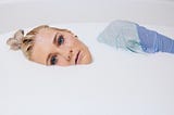 A woman’s face and shoulder showing in a milky bath